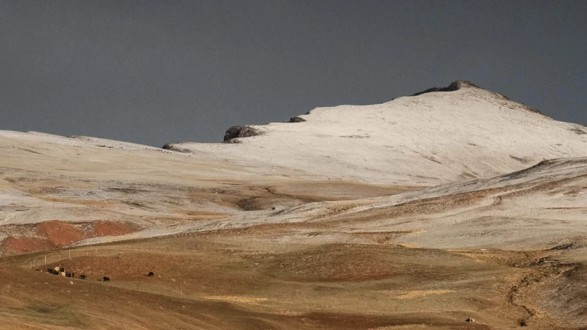 A snow-dusted ridge above a wide golden plateau under a slate-gray sky.